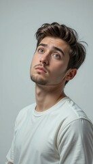 Fototapeta premium Thoughtful young man with striking blue eyes looking up on a plain background