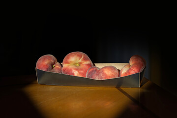 Sunlit Flat Peaches in a Tray on Dark Background