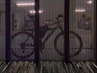 A bicycle is securely parked behind a perforated metal screen on the ground floor of a residential building, highlighting urban living and transportation.