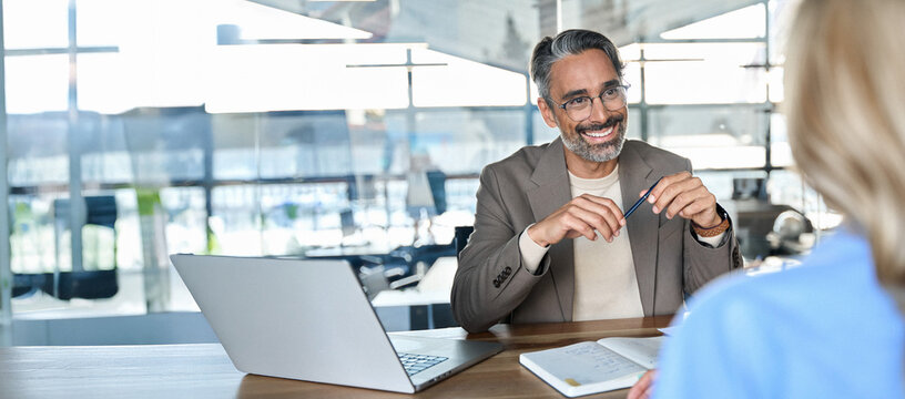 Happy middle aged professional business man executive hr or bank manager, lawyer or financial advisor having job interview or business conversation consulting client at corporate office meeting.