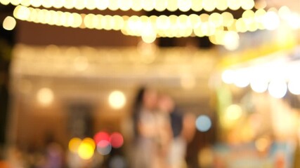A blurry image of a group of people standing outside with lights in the background. Scene is lively and energetic, with the people enjoying each other's company and the festive atmosphere - Powered by Adobe