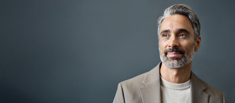 Middle aged business man looking away thinking of future ideas. Smiling confident older mature professional businessman executive ceo manager or entrepreneur standing at gray background. Portrait.