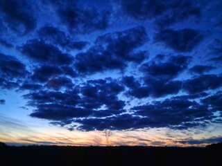 A dramatic sunset sky filled with dark, textured clouds transitions from a deep blue overhead to...