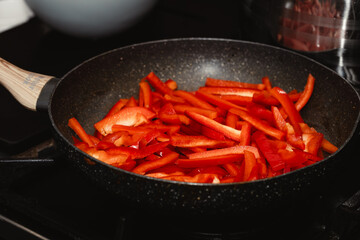 Fresh, Red Peppers Cut Into Stripes, Gently Fried in a Black Pan in a Home Kitchen