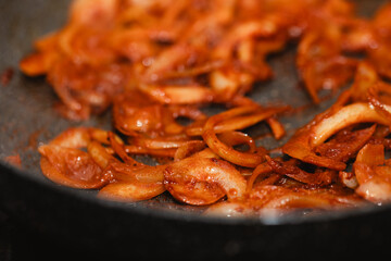 Close-up of frying onions with red pepper powder in a pan, showing texture and intense color