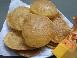 Freshly fried golden pumpkin puris arranged on a paper towel with a raw pumpkin slice on the side,...