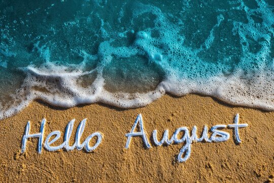 White Hello August text on sand beach under waves of turquoise sea water