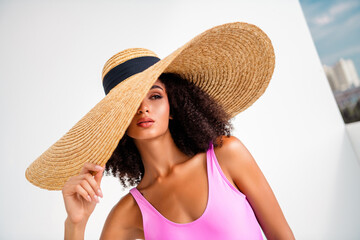 Glamorous young model in oversized straw hat posing confidently in vibrant pink swimwear under...