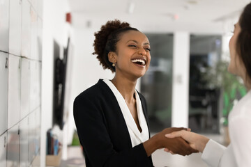 Laughing African businesswoman shaking hands with female colleague, partner or company client,...