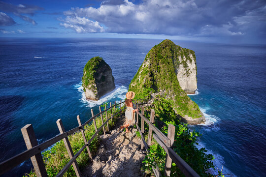 Woman traveler stands on steps of stairs leading to scenic Kelingking beach during a vacation to Nusa Penida Island in Indonesia, explore and travel to touristic beautiful destination