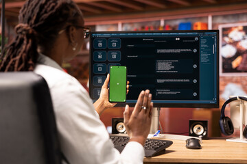 Woman greets friend during videocall on green screen phone in front of PC screen with AI LLM...