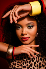 Young woman with stylish makeup and accessories posing against a vivid red background in a...