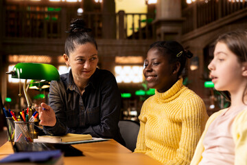 Female professor helping elementary students to practice writing essays and completing homework in...