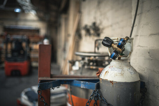 An industrial gas cylinder in a workshop environment with a forklift truck in the blurry background. - Powered by Adobe