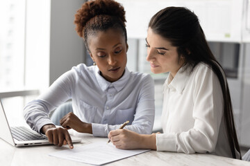 African woman explaining agreement conditions to female, client holding pen signing contract agree on terms, finalize negotiation in office. Accepting new job offer, approving business deal or merger