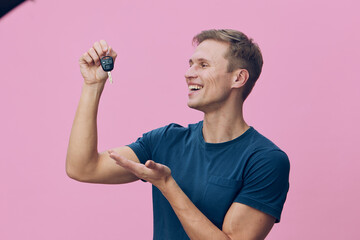Joyful young man holding car key fob and smiling, celebrating success, casual blue t-shirt, pink...
