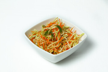 Fresh vegetable salad with cabbage, carrot, and herbs on a plate against a white background