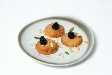Homemade cookies topped with blackberry, almond flakes, and honey on a plate against a white background