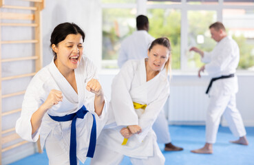 Active middle-aged woman attendee of karate classes practicing fighting techniques during workout...