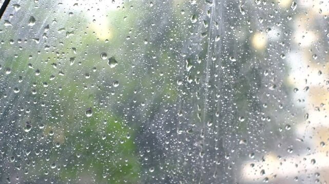 A window with raindrops on it. The raindrops are small and scattered, creating a blurry effect. Scene is calm and peaceful, as the raindrops fall gently on the window