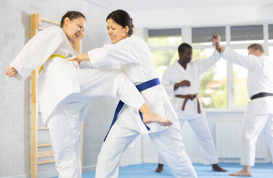 Adult woman and young female judoka practicing judo technique in group in gym