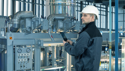 Engineer in hard hat using tablet to inspect industrial equipment at modern factory, monitoring...