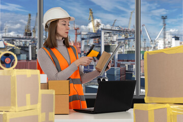 Female worker in safety vest and hard hat scanning packages with barcode scanner at port terminal,...