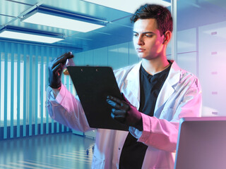 Young male scientist examining a chemical sample and clipboard in a modern laboratory, conducting...
