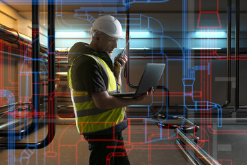 Engineer in safety gear using laptop and radio to inspect and manage complex piping system with digital pipeline overlay. - Engineering. Utilities. Maintenance.