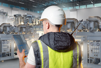 Engineer in safety vest and helmet monitoring industrial machinery with a digital tablet inside a...