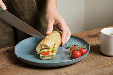 Person Cutting Cheese Veggie Sandwich In Half On Plate