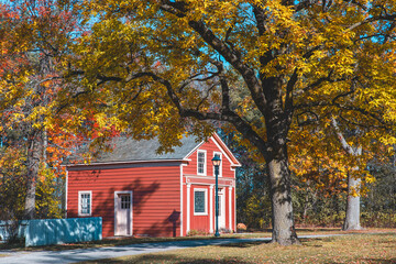 Cozy cabin surrounded by vibrant autumn foliage in a peaceful countryside setting, bathed in warm fall sunlight.