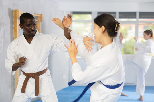 Adult man and young woman judokas practicing judo technique in group in gym