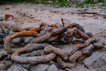 Old rusty metal shipping anchor chains on a sandy bank.