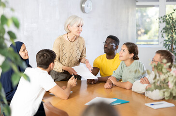 Friendly aged woman conducting language speaking club, communicating with group of adults people of...