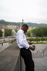 Obraz premium Businessman using smartphone and holding coffee outside during break