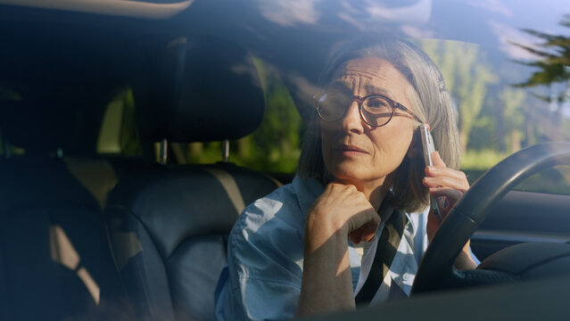 Upset disappointed Caucasian elderly pensioner female driver senior woman sad car owner inside automobile talking mobile phone call cellphone speaking trouble bad news problems negative reaction loss