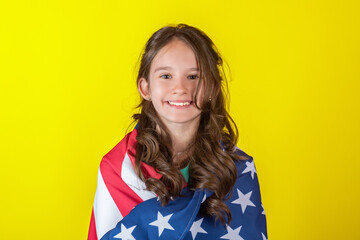Portrait of young smiling cheerful caucasian girl wrapped with American USA flag on yellow...