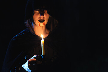 Vampire girl with dripping blood on her mouth and candle in the dark. Halloween theme.