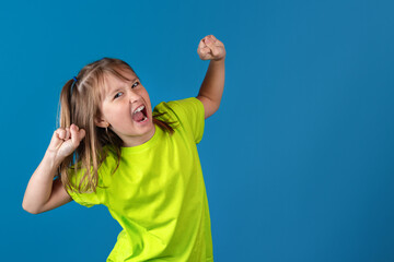 Happy funny young blonde girl posing, fooling around and holding hands up against blue background