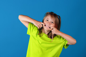 Happy funny young blonde girl posing, making face and fooling around against blue background