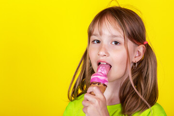 Happy little blonde girl eating ice cream against yellow background. Studio shot