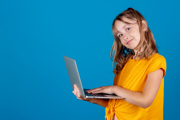 Cute little european smiling girl holding and working with modern silver laptop looking at camera...