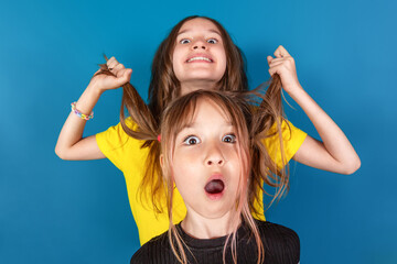 Little girls fooling around. One girl pulls another girl by the hair against blue background....