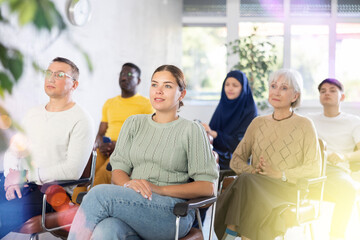 Young woman in casual clothes listens to lecture while sitting on chair in office