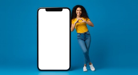 Happy young woman makes heart shape with hands beside giant smartphone with blank screen.