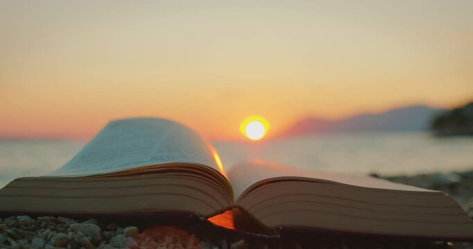 Pages of open book flipping in sea breeze during colorful sunset in summer