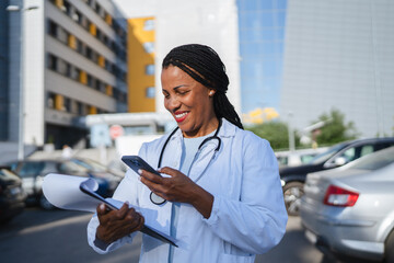 african american woman doctor hold cellphone and scan document outdoor