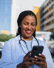 african american woman doctor on break use cellphone in front hospital