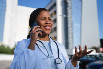 african american woman doctor talk on mobile phone in front hospital